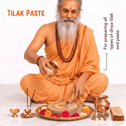 An elderly bearded man in an orange robe sits cross-legged while pouring liquid from a brass pot into a stone grinder on a tray decorated with flowers. The scene includes the text 'TILAK PASTE' and a note explaining use for preparing types of tilak and paste, with brass lamps and a brass vessel nearby on a light background.