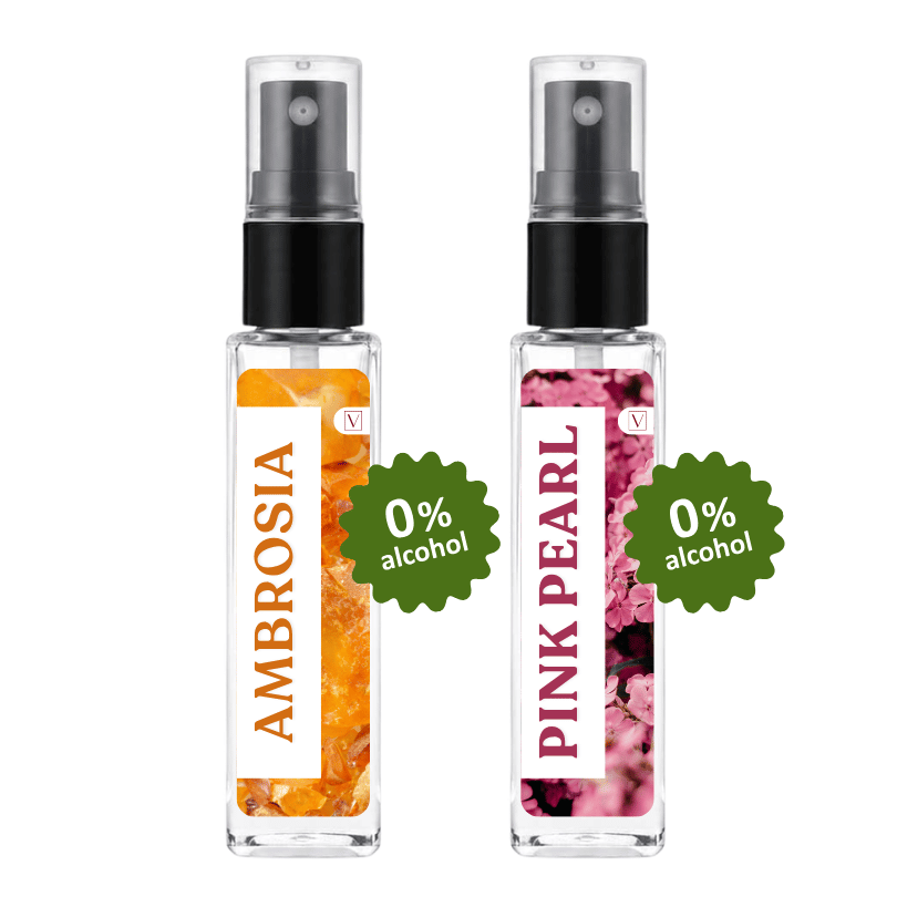 Two clear glass perfume spray bottles with black pumps on a white background. The left bottle is labeled 'AMBROSIA' with an orange honey-like floral design and a green '0% alcohol' badge.