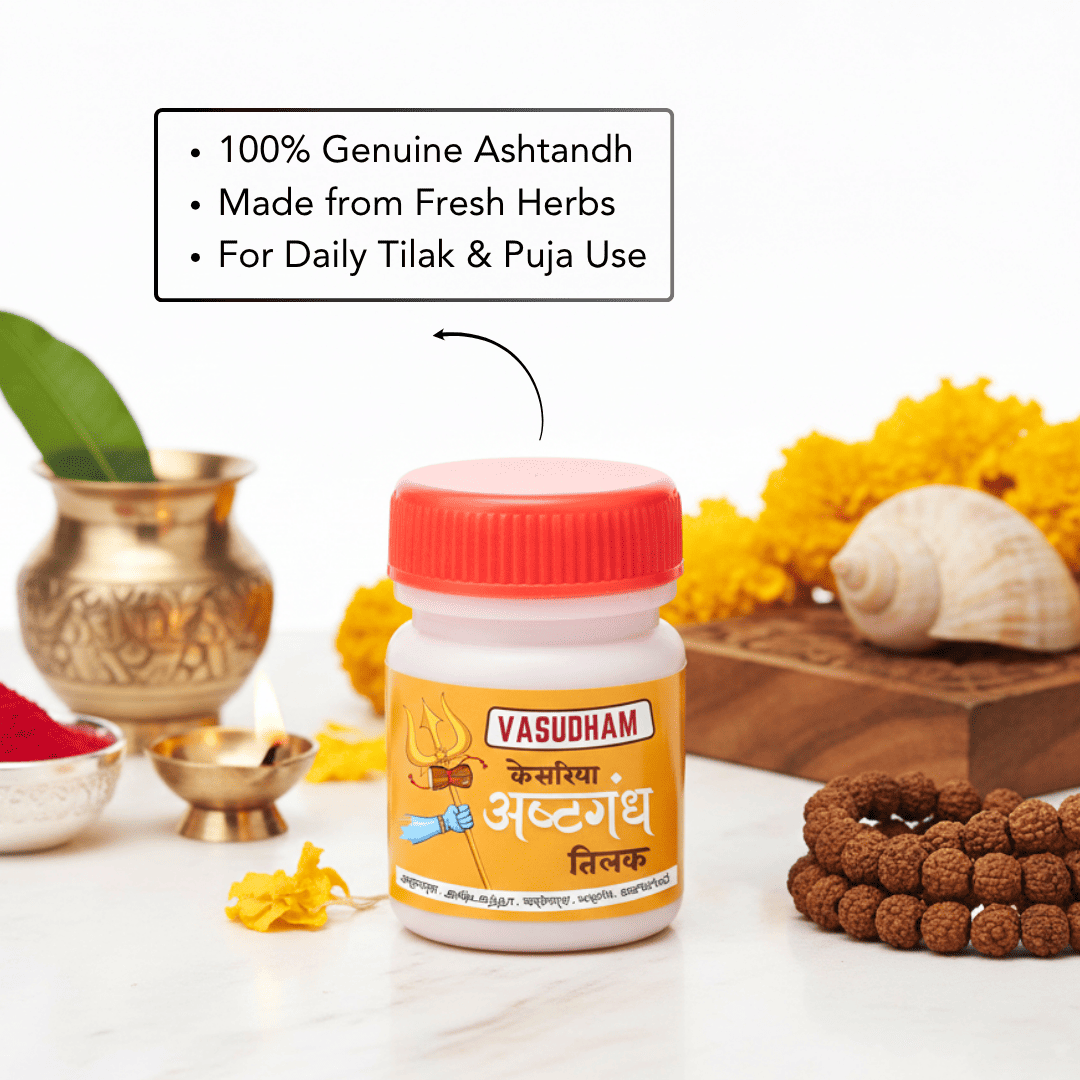 A bottle of Vasudham Ashtgandh Tilak paste centered on a white surface, surrounded by decorative props including a brass pot, yellow flowers, a seashell, a beaded bracelet, and a text callout emphasizing genuine ashtandh and daily tilak use.