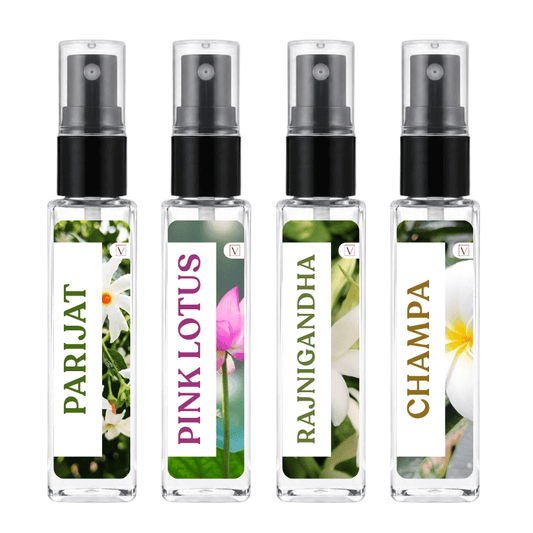 Four clear glass perfume atomizer bottles with black spray pumps, shown side by side on a white background. Each bottle has a floral label with green, pink, white, and gold text reading PARIJAT, PINK LOTUS, RAJNIGANDHA, and CHAMPA.