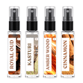 Four clear glass perfume spray bottles with black pump caps, shown side by side on a white background. The labels read ROYAL OUD, KASTURI, AMBER WOOD, and CINNAMON, with warm amber and brown scent imagery on the bottles.