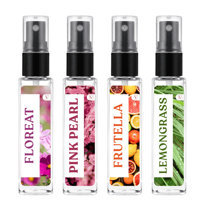 Four clear glass spray bottles with black pumps and clear caps, arranged side by side on a white background. Each bottle has a vertical white label with a different scent illustration: FLOREAT with pink flowers, PINK PEARL with pink blossoms, FRUTELLA with citrus fruits, and LEMONGRASS with green leaves.