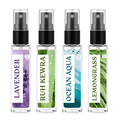 Four small clear spray bottles with black pump tops arranged side by side on a white background. Each bottle has a different botanical label: lavender purple, green-leaf Ruh Kewra, blue-green Ocean Aqua, and green Lemongrass.
