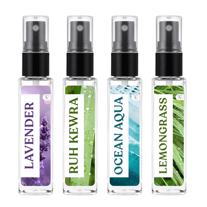 Four small clear spray bottles with black pump tops arranged side by side on a white background. Each bottle has a different botanical label: lavender purple, green-leaf Ruh Kewra, blue-green Ocean Aqua, and green Lemongrass.