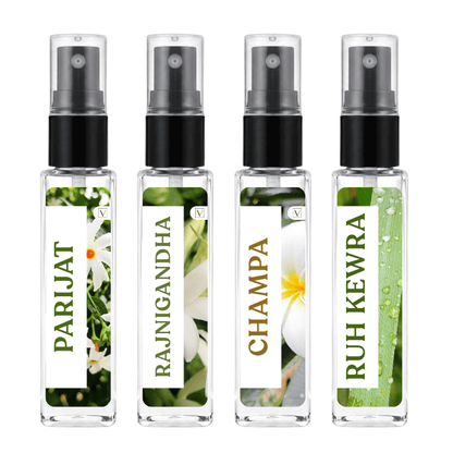 Four clear glass perfume atomizer bottles with black spray nozzles, arranged side by side on a white background. Each bottle has a white label with green and gold text and a floral or natural print: PARIJAT, RAJNIGANDHA, CHAMPA, and RUH KEWRA.