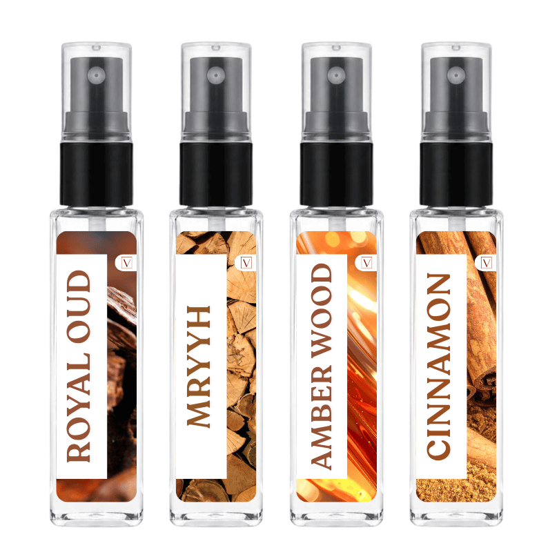 Four small clear glass spray bottles with black pump tops, arranged side by side on a white background. Each bottle has a different warm-toned label reading ROYAL OUD, MRYYH, AMBER WOOD, and CINCINN, with wood and amber imagery behind the text.