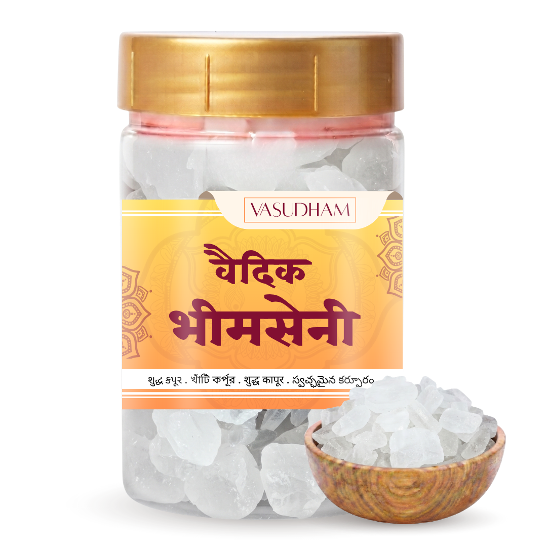 A clear plastic jar of Vasudham bhimseni camphor with a gold lid and orange label, shown next to a small wooden bowl filled with the clear, translucent stones on a white background.