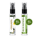 Two clear glass perfume spray bottles with black atomizers on a white background. The left bottle has a white label with 'CHAMPA' in gold text and a white flower photo, with a green starburst reading '0% alcohol'.