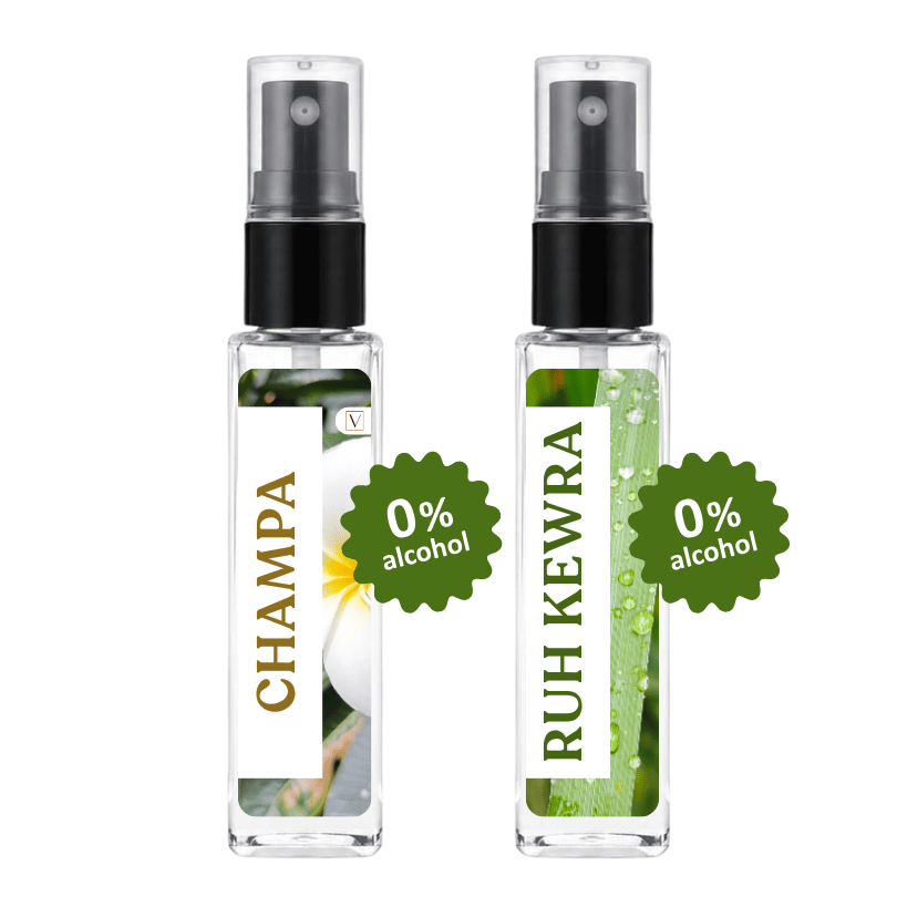 Two clear glass perfume spray bottles with black atomizers on a white background. The left bottle has a white label with 'CHAMPA' in gold text and a white flower photo, with a green starburst reading '0% alcohol'.