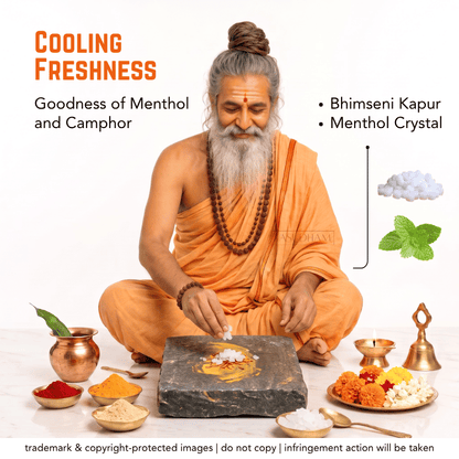 A man with a long gray beard and hair in a bun, dressed in orange robes, sits cross-legged on a white background while preparing a paste on a dark stone slab. Surrounding him are small bowls of colorful powders, a copper pot with a leaf, a brass lamp, and a plate of marigolds, flowers, and crystals.