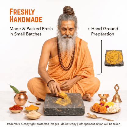 A man with a long gray beard and hair in a bun, dressed in orange robes, sits cross-legged while grinding yellow turmeric powder on a dark stone slab. Surrounding him are bowls of spices, marigolds, a brass bell, and decorative items on a white studio background, with text reading 'Freshly Handmade' and 'Hand Ground Preparation'.