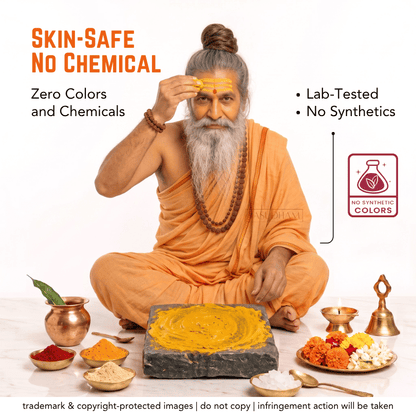 An elderly man with a long white beard and hair in a bun, dressed in orange robes, sits cross-legged while applying a yellow paste to his forehead. In front of him is a stone slab with more yellow paste, surrounded by small bowls of colorful powders and brass lamps.