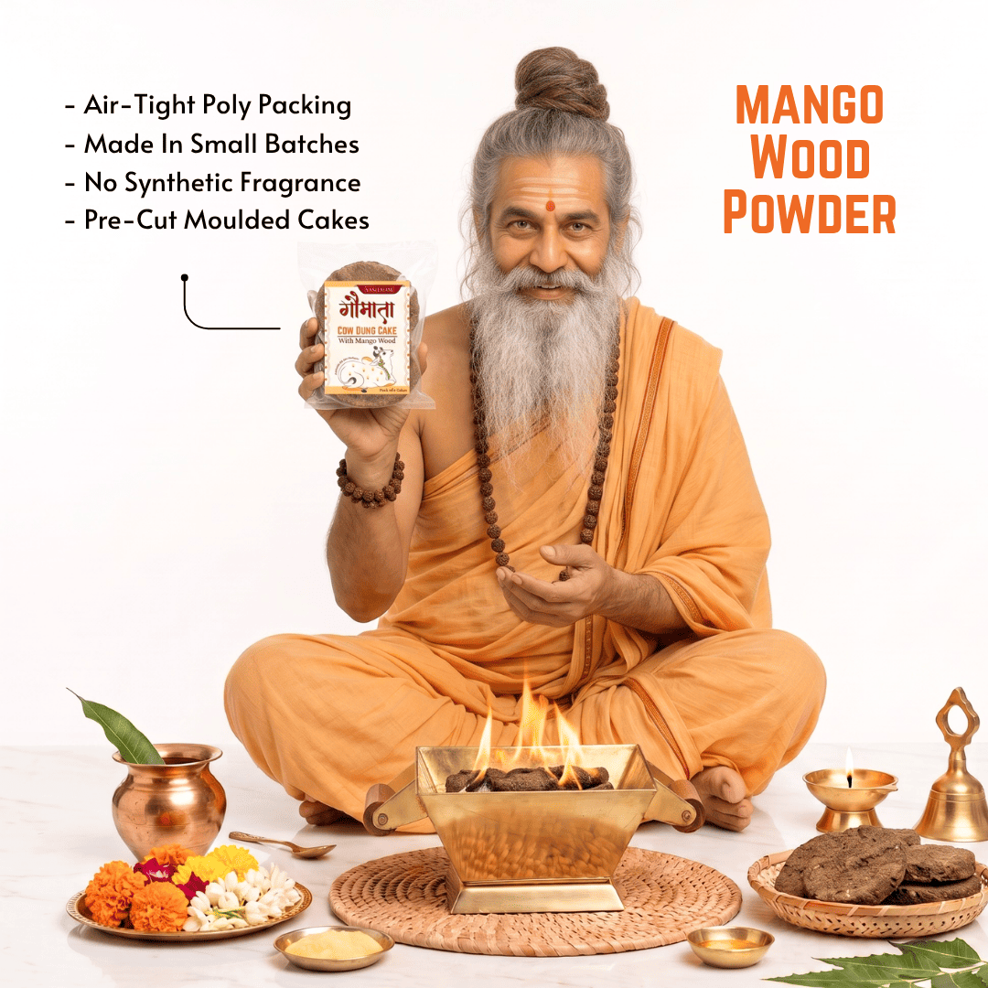 An elderly man with a long gray beard and hair in a bun, dressed in orange robes, holds up a jar of Mango Wood Powder. The scene is set on a white background with traditional Indian elements, including a brass incense burner with flames, a copper pot, marigolds, and cookies.