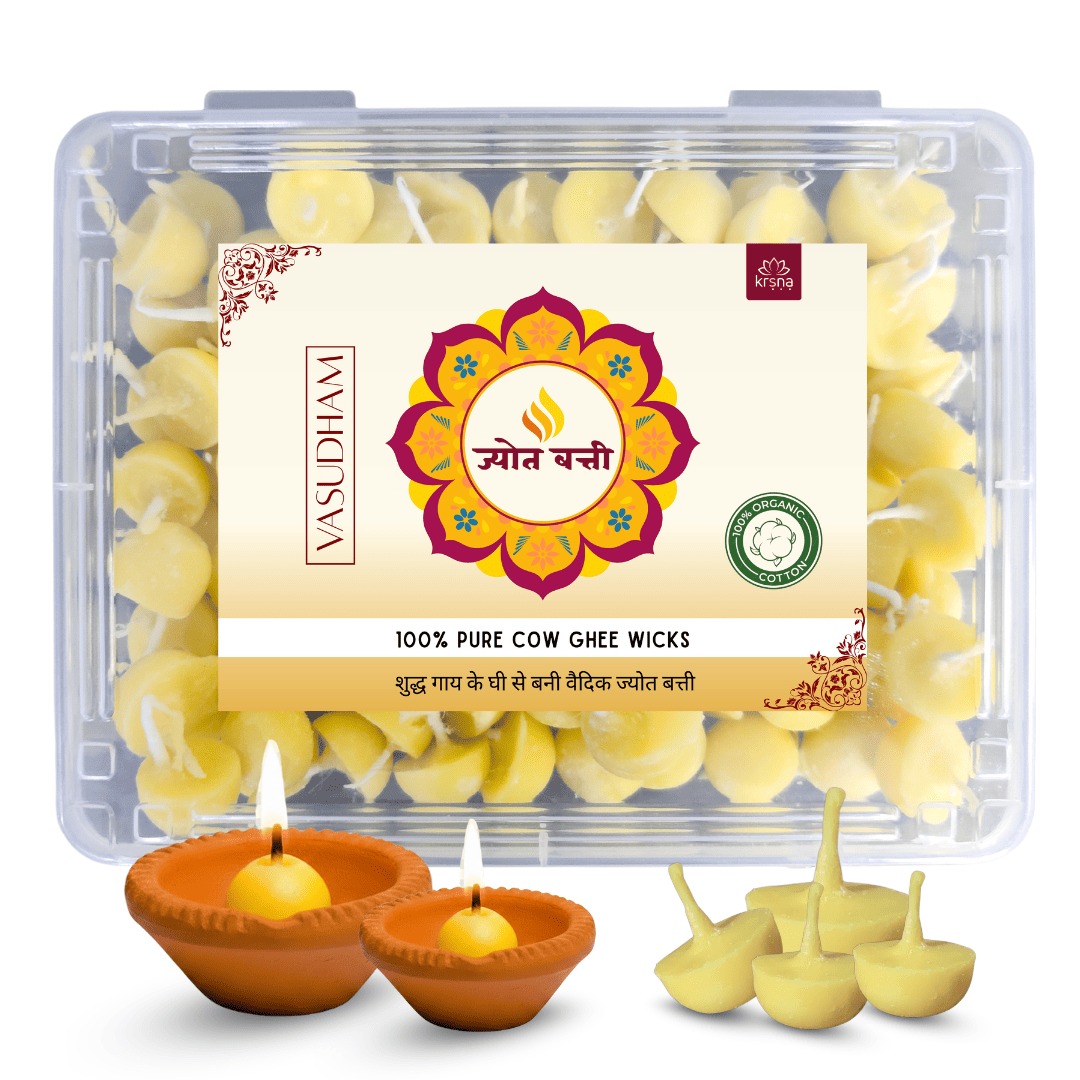 A clear plastic box of Vasudham 100% Pure Cow Ghee Wicks with a cream-colored label, shown alongside two lit clay diya lamps and several unlit yellow ghee wicks on a white background.