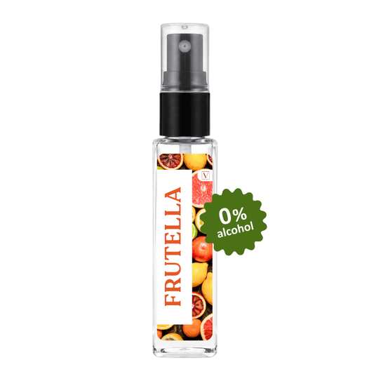 A clear glass perfume atomizer bottle with a black spray pump, featuring a white label with red 'FRUTELLA' text and a colorful citrus and fruit print. A green circular badge on the right reads '0% alcohol'.