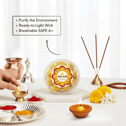 A clear round container of yellow flower light sticks sits on a white marble board on a table, surrounded by ritual props including a brass incense holder, copper bells, a diya, and a hand lighting a small flame. Text on the image lists product features.