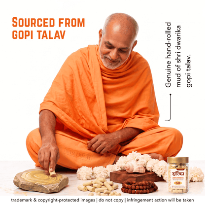 A man in an orange robe sits cross-legged on a white background, touching a circular mud sample. In front of him are loose nuts, a jar of Gopi Talav mud, and a wooden tray with reddish-brown beads.