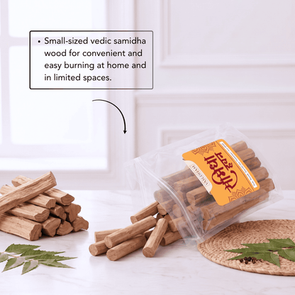 A clear plastic bag of small wooden samidha sticks with an orange label, shown tipped over on a light surface with several sticks spilled out. More wood pieces are stacked on the left, with a text callout explaining they are small-sized vedic samidha wood for convenient burning.