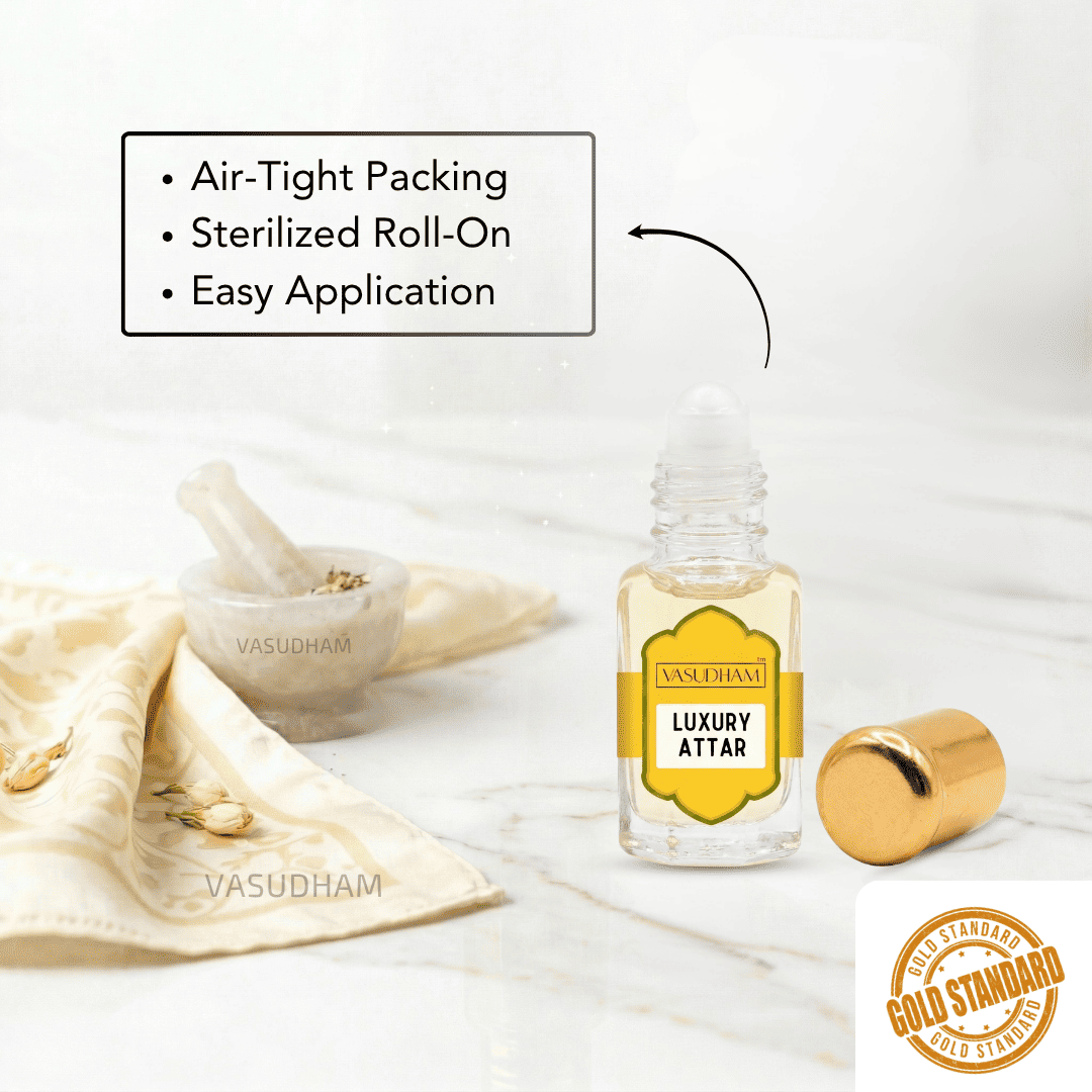 A clear glass roll-on bottle labeled 'VASUDHAM LUXURY ATTAR' with a yellow label and gold cap, shown on a light marble surface with a gold cradle and a folded cream cloth. Text highlights air-tight packing, sterilized roll-on, and easy application.