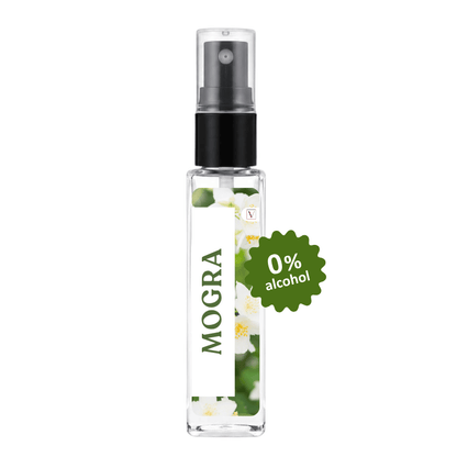 A clear glass perfume spray bottle with a black pump and a white label featuring the brand name 'MOGRA' and white jasmine flowers. A green starburst badge on the right reads '0% alcohol'.