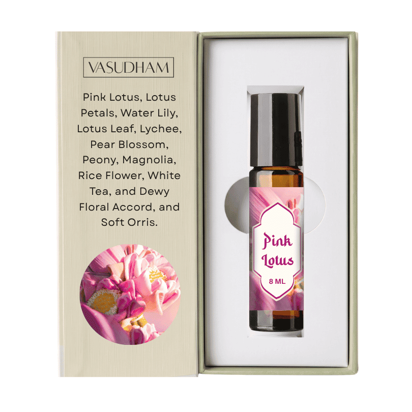 Vasudham Pink Lotus essential oil roller bottle in its original presentation box. The 8 ml amber glass bottle with a black cap is nestled inside a white insert next to its beige outer packaging, which features a pink lotus flower graphic and a list of scented ingredients.