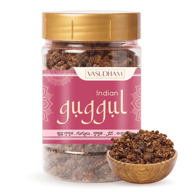A jar of Vasudham Indian Guggul herbal powder with a gold lid and a pink label, shown alongside a small wooden bowl filled with the dark brown powder on a white background.