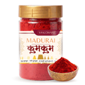 A jar of Vasudham Madurai Kumkum (red Indian henna) with a gold lid and a white label, shown alongside a small wooden bowl filled with the red powder on a white background.