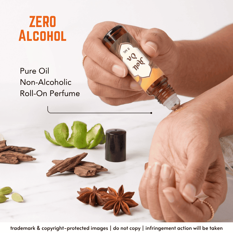A person's hands squeeze a roll-on perfume bottle labeled 'Joel 04' onto a skin surface, with text reading 'ZERO ALCOHOL' and 'Pure Oil Non-Alcoholic Roll-On Perfume.' Spices and citrus slices are arranged on a white surface around the bottle.