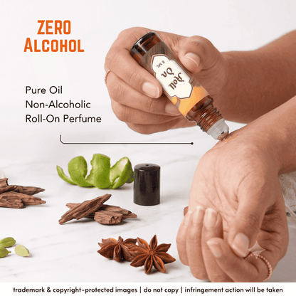A person's hands squeeze a roll-on perfume bottle labeled 'Joel 04' onto a skin surface, with text reading 'ZERO ALCOHOL' and 'Pure Oil Non-Alcoholic Roll-On Perfume.' Spices and citrus slices are arranged on a white surface around the bottle.