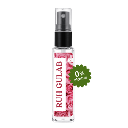 A clear glass perfume spray bottle with a black pump, featuring a pink rose pattern label and the brand name 'RUH GULAB' printed vertically. A green circular badge on the right reads '0% alcohol'.