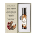 Vasudham Saffron Oud essential oil roller bottle in an amber glass bottle with a black cap, presented inside its white packaging insert next to the beige outer box with product details and a botanical illustration.