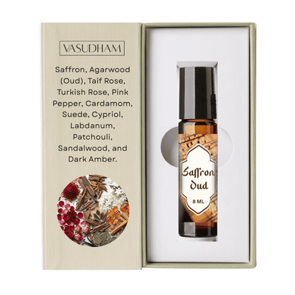 Vasudham Saffron Oud essential oil roller bottle in an amber glass bottle with a black cap, presented inside its white packaging insert next to the beige outer box with product details and a botanical illustration.