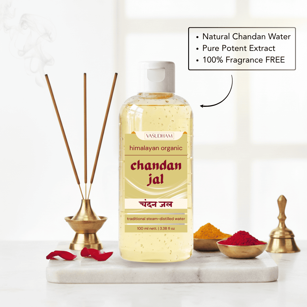 A bottle of Vanshrami Chandan Jal traditional steam-distilled water placed on a white marble tray with incense sticks, red rose petals, and small bowls of yellow and red powders. A text box highlights natural chandan water, pure potent extract, and 100% fragrance free.