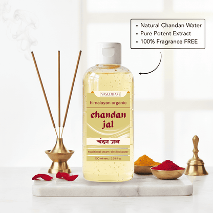 A bottle of Vanshrami Chandan Jal traditional steam-distilled water placed on a white marble tray with incense sticks, red rose petals, and small bowls of yellow and red powders. A text box highlights natural chandan water, pure potent extract, and 100% fragrance free.