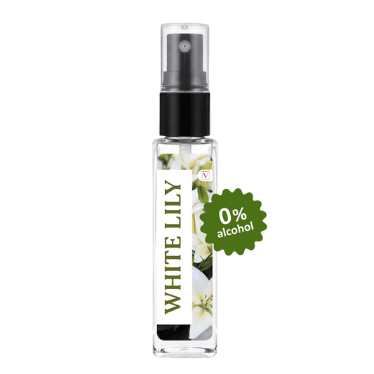 A clear glass perfume or body spray bottle with a black pump, labeled 'WHITE LILY', featuring white lily flowers on the front. A green badge on the right reads '0% alcohol'.