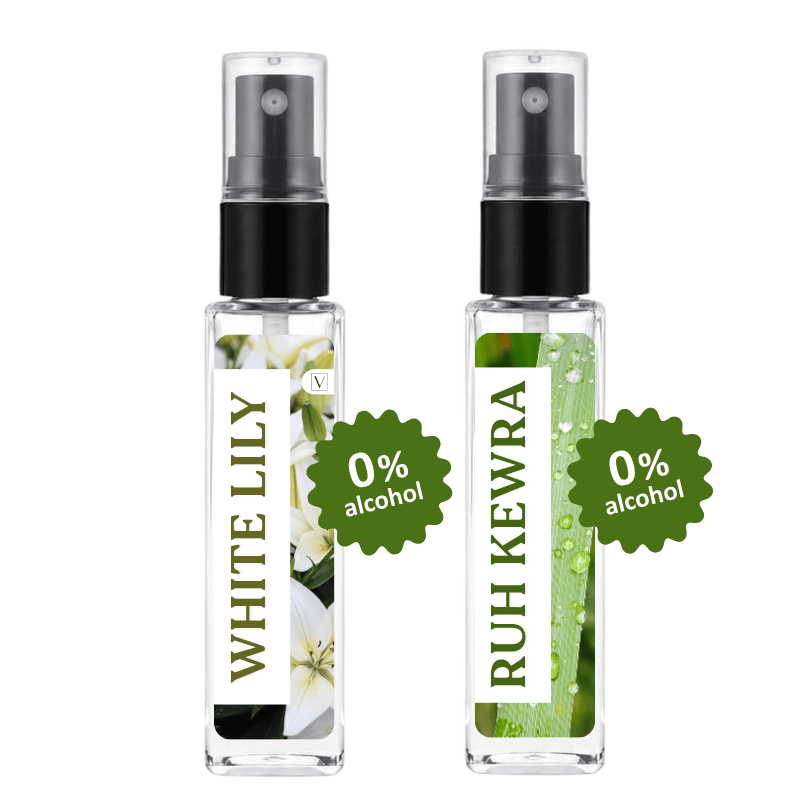 Two clear glass perfume spray bottles with black pumps on a white background. The left bottle has a white label with green text reading 'WHITE LILY' and white flower imagery, with a green starburst sticker reading '0% alcohol'.